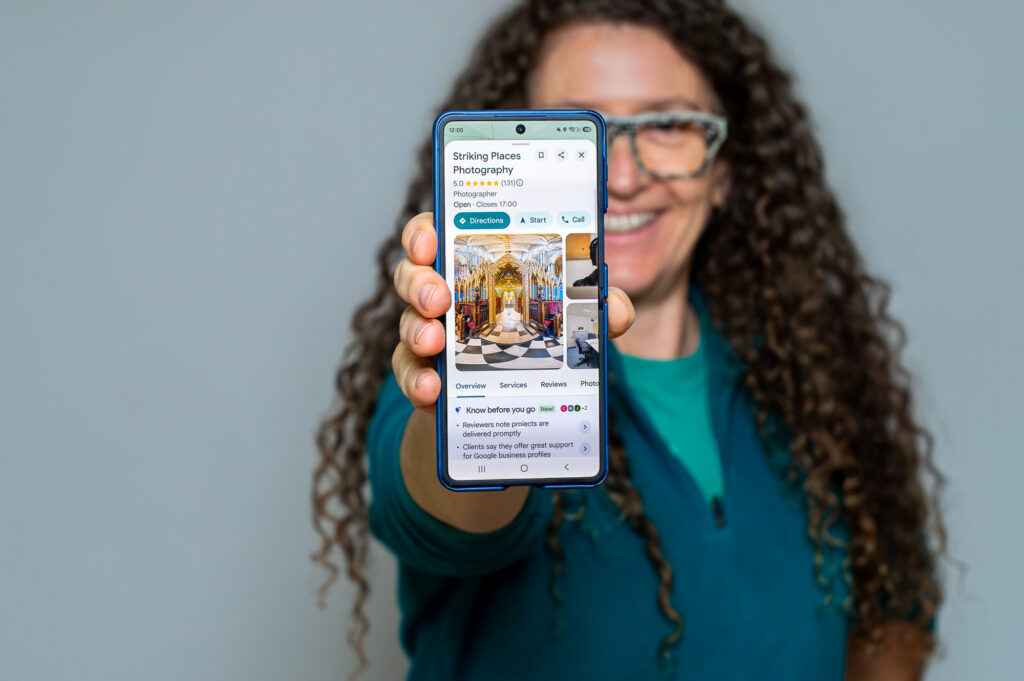 Jo Hailey holding a phone showing the Striking Places Google Business Profile with 5 stars from 131 reviews