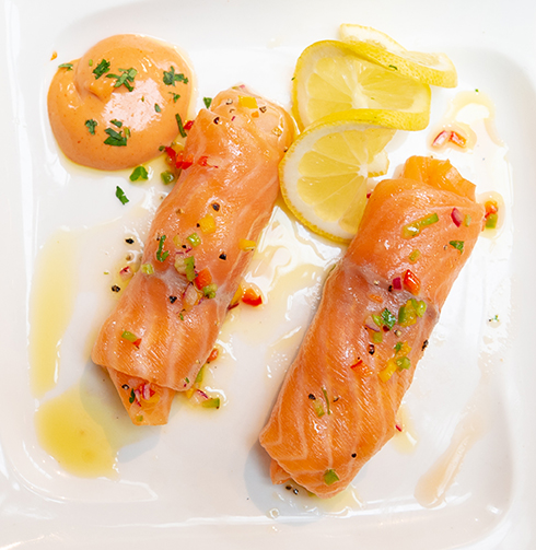 Smoked salmon rolled on a white plate with twirled lemon and a blob of rose marie sauce